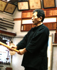 A Japanese man dressed in black holds a fighting practice baton.