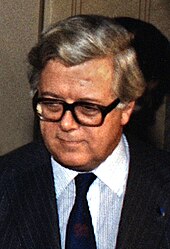 A silver-haired man in a black suit and tie