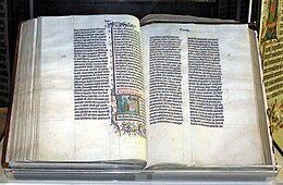 A large old Bible, open and displaying two pages of densely-written calligraphy, with some decoration surrounding one section on the left-hand page.