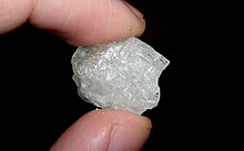 A shiny translucent white crystal of methamphetamine, held between the ends of a finger and thumb