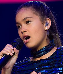 A close-up photo of Curtis holding a microphone while wearing a blue outfit