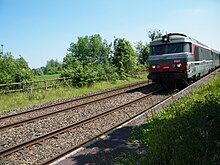 Passage d'un train près du quai de l'ancienne gare, par temps ensoleillé.