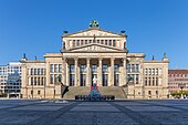 Farbfotografie eines klassizistischen zweigeschossigen Gebäudes mit Säuleneingang und Giebelfeld. Ein weiteres Geschoss mit Giebelfeld und Quadriga befindet sich in der Mitte. Breite Stufen führen zum Vorplatz mit einer Marmorfigur.