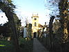 Yellow stone building with prominent square tower. Trees to left and right of the path leading to the building.