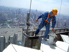 Window cleaner climbing out of a scaffold equipped with height harness and a fitted hardhat.