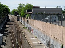 Disused platforms next to an active railway line in a cut, with a one-story midcentury building at right