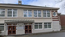 A wide, two floor building with many latticed windows has a sign that says "3203, Community History Centre, North Vancouver Museum and Archives Commission". There are two entrances with brown, wooden doors, with each door having two glass panels to see into the lobby area.