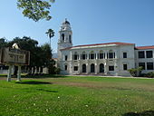 A stately old school building with a clock tower, seen across a large green lawn