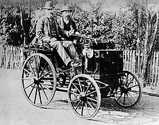 Photo d'une voiture d'apparence hippomobile avec un chauffeur et un passager.