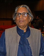 Photograph of an old man wearing a blue-coloured jacket and glasses.