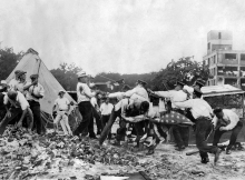 Police with batons confront demonstrators armed with bricks and clubs. A policeman and a demonstrator wrestle over a US flag.