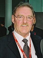Kevin Beattie wearing a dark jacket, a white shirt, and black-and-white polka dot tie