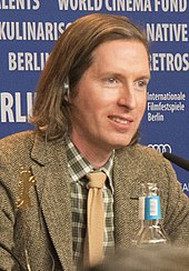 A bob-haired man sitting at a movie conference