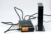 Hardware (a plug computer, yellow, a wireless router, and a USB drive carrying a fresh copy of the French Wikipedia) used in the Afripedia project Afripedia hardware n02.jpg