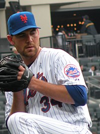 A man in a white pinstriped baseball uniform and blue cap winds up to throw a baseball.