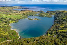 Une baie, aux eaux transparentes, entourée d'arbres et de champs, son accés à la mer barré par des îles ou presqu'îles.