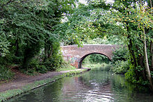 red bricked bridge over a small canal, surrounded in green