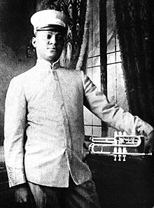 Dieses Foto in schwarzweiß zeigt den US-amerikanischen Jazzmusikern und Kornettspieler Freddie Keppard stehend als frontale Aufnahme bis zum Gesäß von vorne mit seinem Musikinstrument Kornett in der linken Hand an und wurde 1908 aufgenommen.