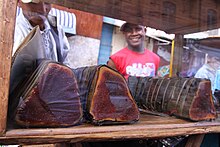 Thick, dark brown rolls of koba, a peanut pate wrapped in banana leaves. Here it is being sold by street vendors in Antananarivo, Madagascar. Kobandravina dessert snack food Antananarivo Madagascar.jpg