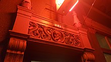 Photograph of architectural detail of a building's exterior, illuminated by a neon sign