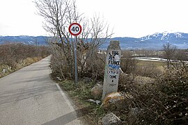 Vue d’une borne au bord d’une route, devant un panneau de limitation de vitesse.