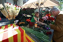 A young person sells a rose to an elderly person at a rose stall. Sounded by roses and an white umbrella for shade.