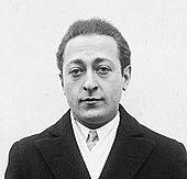 head and shoulders shot of a man in overcoat, jacket and tie, looking at the camera