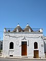 Trullo house with raised façade wall hiding both its conical roofs (Alberobello)