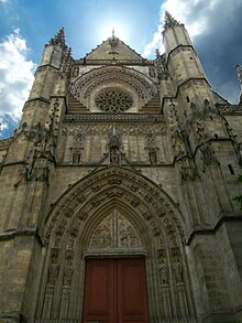 Photographie de la Basilique saint Michel. Un haut bâtiment en pierre situé sur une large place piétonne.