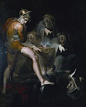 Macbeth, barefoot and wearing body paint or armour and short trousers reaches into an iron pot with three old men in it. They are looking at Macbeth and pointing fingers a figure below.