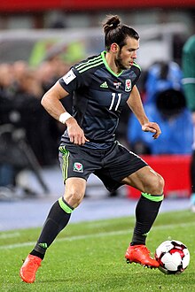 A footballer wearing a black jersey and black shorts attempts to dribble a football.