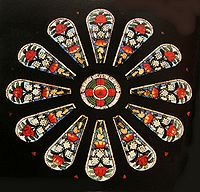 a small round stained glass window surrounded by twelve panels featuring floral designs of large red and small white flowers