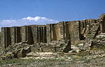 A picture of a deteriorating stone wall spanning the frame, with a blue sky in the background.