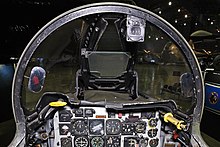 A view from the front seat of an F-100F cockpit, looking directly forward. The view outside is partially obscured by metal canopy supports.