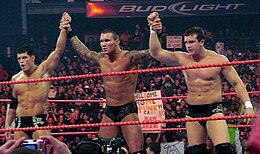 Trois catcheurs se tiennent debout dans un ring, torses nus, vêtus uniquement d'un slip noir. Ils se tiennent par la main et lèvent le bras en signe de victoire. De gauche à droite : Cody Rhodes, Randy Orton et Ted Dibiase, les trois principaux membres du clan.