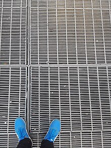 close up view of subway grating with the photographer's shows in view for scale.