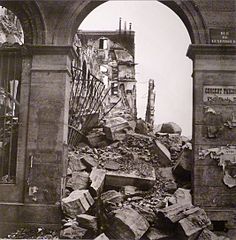 Arcade grise encombrée de gravats derrière laquelle on voit des ruines.