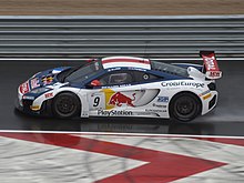 McLaren MP4-12C GT3 de couleur bleue et blanche, vue de profil sur une piste goudronnée détrempée.