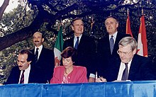 Photographie des premiers ministres du Canada, des États-Unis et du Mexique debout derrière les trois ministres du Commerce international de ces pays, signant l'Accord de libre-échange nord-américain.