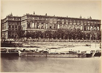 Au premier plan un fleuve. A l'arrière plan un grand bâtiment rectangulaire gris dont il ne reste que les façades.