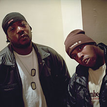 Two African-American men, in white shirts, black jackets and skullcaps, pose for a photograph.