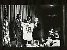 Ed "Too Tall" Jones and Harvey Martin present President Gerald R. Ford with a football jersey at the Texas Stadium Club, April 9, 1976.
