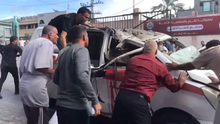 Men surrounding a bombed vehicle. There is some blood streaking it.