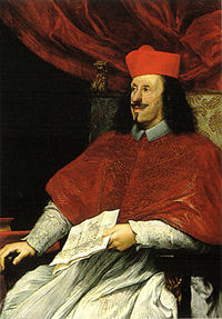 A black-haired, bearded man in his mid-thirties wears the garb of a cardinal.