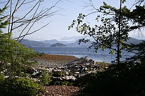 A pebble beach along the water with mountains visible in the far distance