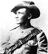 Black and white photograph of Breaker Morant. He is facing to the left of the photograph, showing his side profile. He is wearing a slouch hat and has an ammo belt strapped across his chest and over his left shoulder.