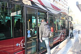 Un bus arrêté, un voyageur monte par une porte arrière