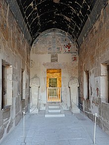 Hall with a vaulted ceiling, all covered in painted artwork, and a pair of stone statues