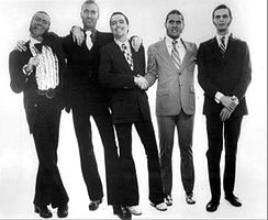 Promotional photo of all five members, wearing tuxedos and grinning.