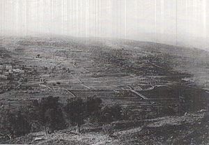 Landscape photo taken from high hill shows two villages and fields with a road crossing in the middle distance from left to right of the photo.